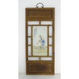 A Chinese wooden wall hanging with an porcelain panel depicting a man with books at his feet.