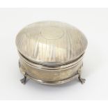 A silver ring box with engine turned decoration and standing on three feet.