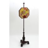 A Victorian mahogany pole screen with an adjustable needlework top and standing on a tapering stem