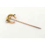 A 9ct gold stick pin / stock pin surmounted by a horseshoe and riding whip / crop