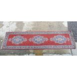 Carpet / Rug: a hand made woollen runner with red central ground having 3 oval shaped blue and buff