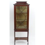 An early 20thC mahogany display cabinet with a raised up stand above an astragal glazed door and