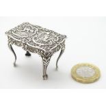 Silver dolls house furniture : A miniature silver table with floral scroll and cherub decoration on