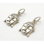 A pair of white metal charms / pendants formed as Buddha heads.