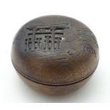A small turned wooden pot and cover of circular form with carved decoration depicting an oriental