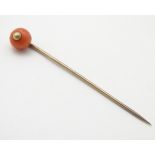 A gold stick pin surmounted by a coral cabochon. Approx. 3” long.