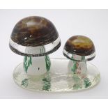 A coloured glass paperweight in the form of two toadstools/mushrooms upon a clear glass vase,