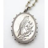 A white metal locket of oval form with engraved decoration depicting a song bird on a branch.