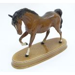 A Beswick horse with a leg raised and head tucked standing on an oval ceramic base. Marked under.