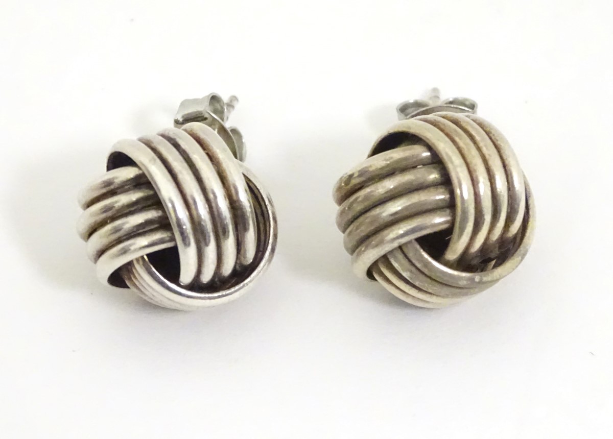 A pair of white metal stud earrings formed as large knots.