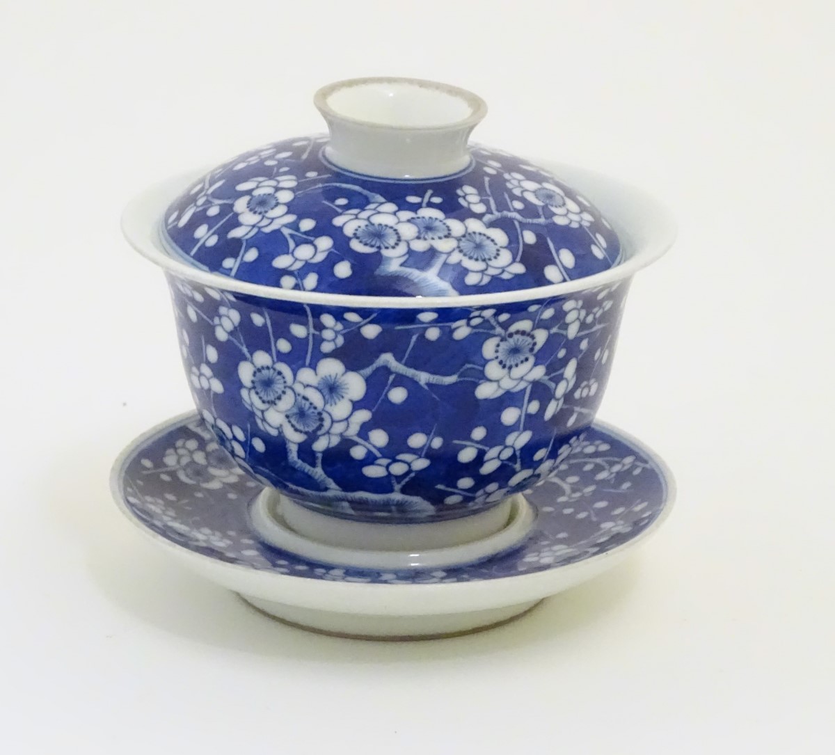 A Chinese blue and white tea bowl, lid and saucer, decorated with cherry blossom.