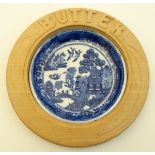 A blue and white ceramic 'Willow' pattern butter dish in carved wooden surround. 6'' diameter.
