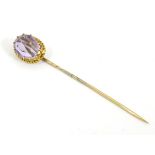A yellow metal (tests as 9ct gold) stick pin surmounted by a facet cut amethyst.