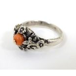 A silver ring set with central coral bead within a floral mount.