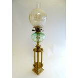 An oil lamp with a brass stand supporting a green glass oil reservoir and globular shade.