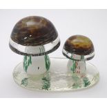 A coloured glass paperweight in the form of two toadstools / mushrooms upon a clear glass vase,