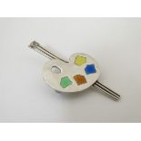 A silver brooch formed as an artist's palette and brushes, the palette with enamel paint detail.