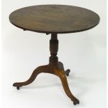 A Georgian oak tilt top table with a circular top above a tapering turned stem and a tripod base