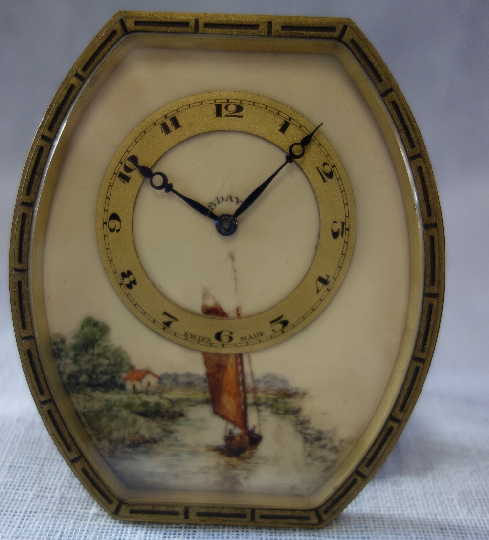 A 1920S BEDSIDE CLOCK in a brass case, the face painted with a boat on a river, 10cm high