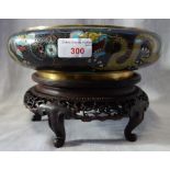 A CLOISONNE BOWL decorated with dragons on a black ground, 25cm dia. on a carved wooden stand