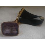 A 9CT YELLOW GOLD FOB set with 'amethyst' attached to black ribbon