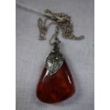 AN "AMBER" PENDANT, with white metal leaf surmount, attached to a silver fine link chain