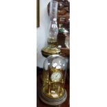 A BRASS ANNIVERSARY CLOCK under a glass dome and a brass oil lamp