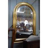 A GILT FRAMED WALL MIRROR with arched bevelled plate