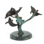 Naturalistic patinted bronze sculpture of three dolphins, raised on a circular green marble base,