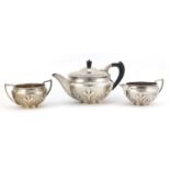 Arts & Crafts style silver three piece tea service embossed with stylised motifs, the teapot with