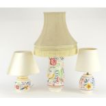 Three Poole pottery lamp bases with shades, each hand painted with flowers, the largest overall 62cm