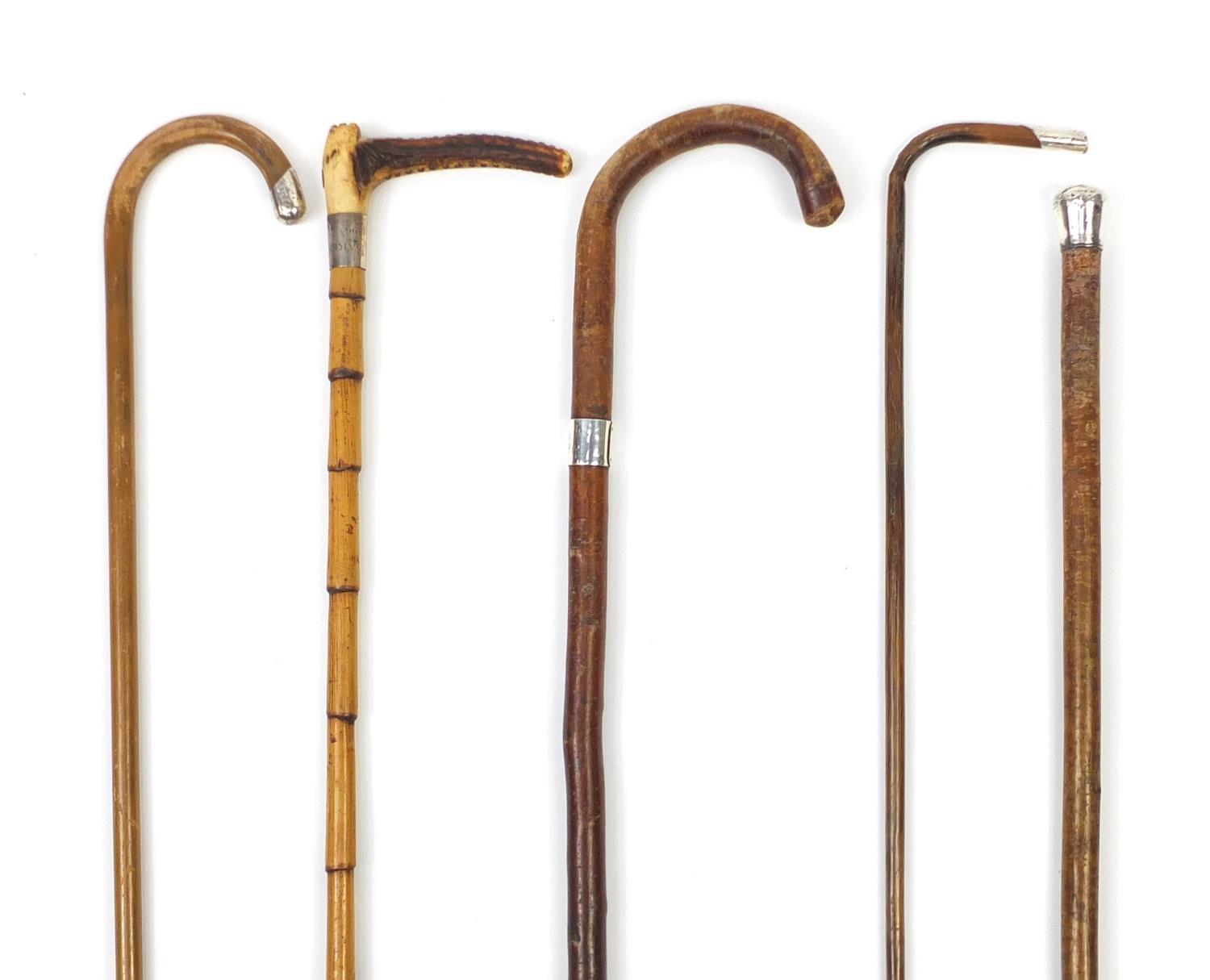 Four walking sticks with silver mounts and a Swain and Co silver mounted riding crop, the largest