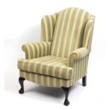 Mahogany framed wingback armchair with green and gold upholstery, raised on ball and claw feet,