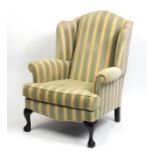 Mahogany framed wingback armchair with green and gold upholstery, raised on ball and claw feet,
