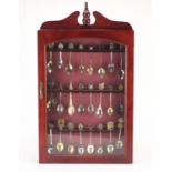 Collection of souvenir teaspoons including some silver and some enamelled, housed in a display case,