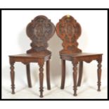 A pair of 19th century armorial carved oak hall chairs each being raised on turned tapering legs