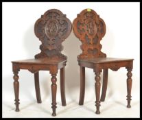 A pair of 19th century armorial carved oak hall chairs each being raised on turned tapering legs