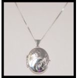 A stamped 375 white gold necklace with a spring ring clasp having a oval form locket with foliate