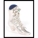 A silver pincushion in the form of a Victorian lace up boot having a blue cushion and green stone to