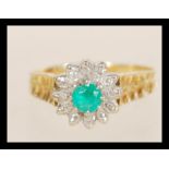 A stamped 18ct gold emerald and diamond cluster ring set with a central emerald surrounded by a