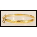 A 9ct gold B-Core bracelet bangle having diamond cut decoration with clip clasp and safety chain.