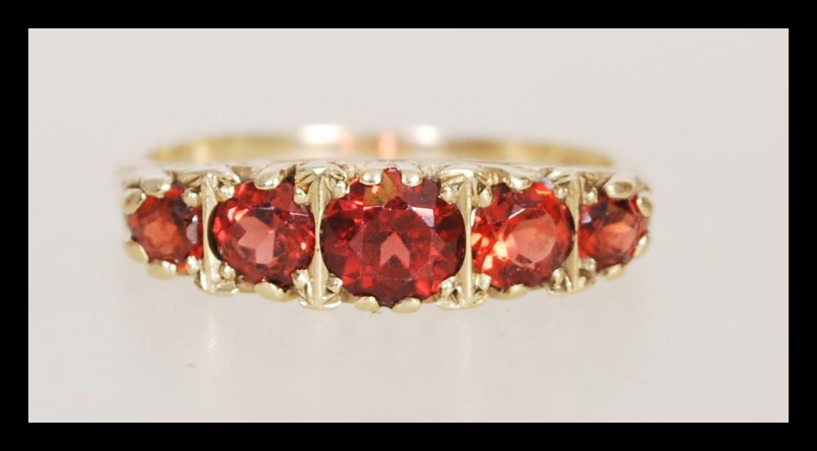 A hallmarked 9ct gold five stone ring having graduating faceted red stones in scrolled mount. Weighs