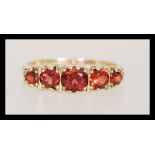 A hallmarked 9ct gold five stone ring having graduating faceted red stones in scrolled mount. Weighs