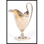 An early 20th century silver hallmarked creamer milk jug raised on square plinth base with shaped