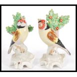 A pair of early 20th Century Staffordshire type figurines depicting goldfinches raised on