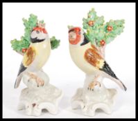 A pair of early 20th Century Staffordshire type figurines depicting goldfinches raised on