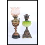 Two early 20th Century oil lamps to include a brass round base example with a pink glass shade to
