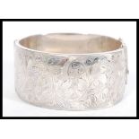 A silver hallmarked bangle bracelet having foliate engraving, with a hinged opening and safety