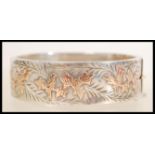 A large silver hallmarked bangle bracelet having engraved  and gold leaf design with safety chain.