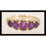 A hallmarked 9ct gold ring set with five oval purple stones with decorative scrolled shoulders.